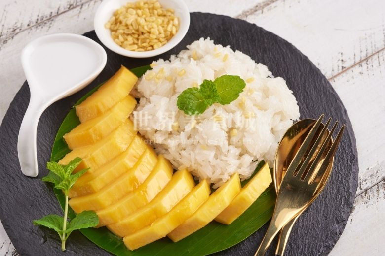 mango sticky rice put on a black stone plate with golden fork and spoon