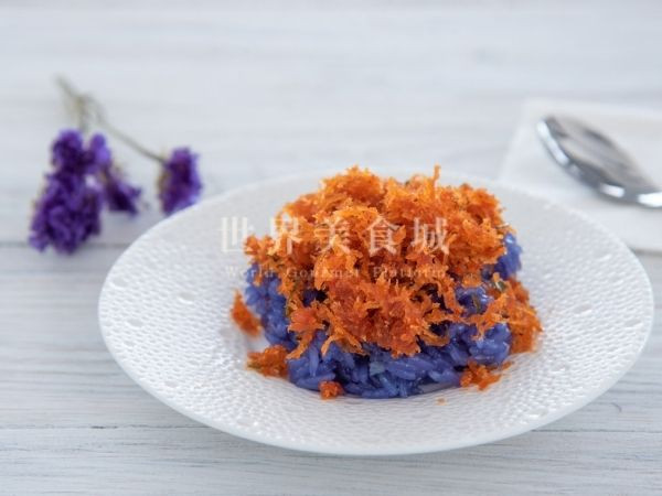 Shrimp sticky rice with attached spoon and small bouquet of purple flowers on the side